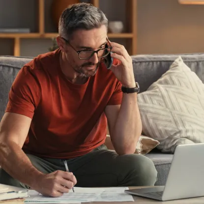 Man on couch using his phone with his laptop 